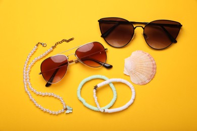 Stylish sunglasses, accessories and seashell on yellow background, flat lay