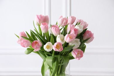 Photo of Beautiful bouquet of tulips in glass vase against white wall