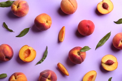 Photo of Fresh ripe peaches and green leaves on violet background, flat lay