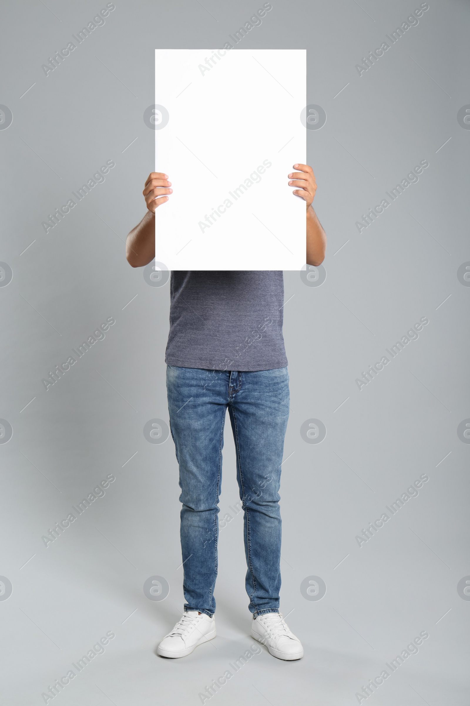 Photo of Man holding white blank poster on grey background. Mockup for design