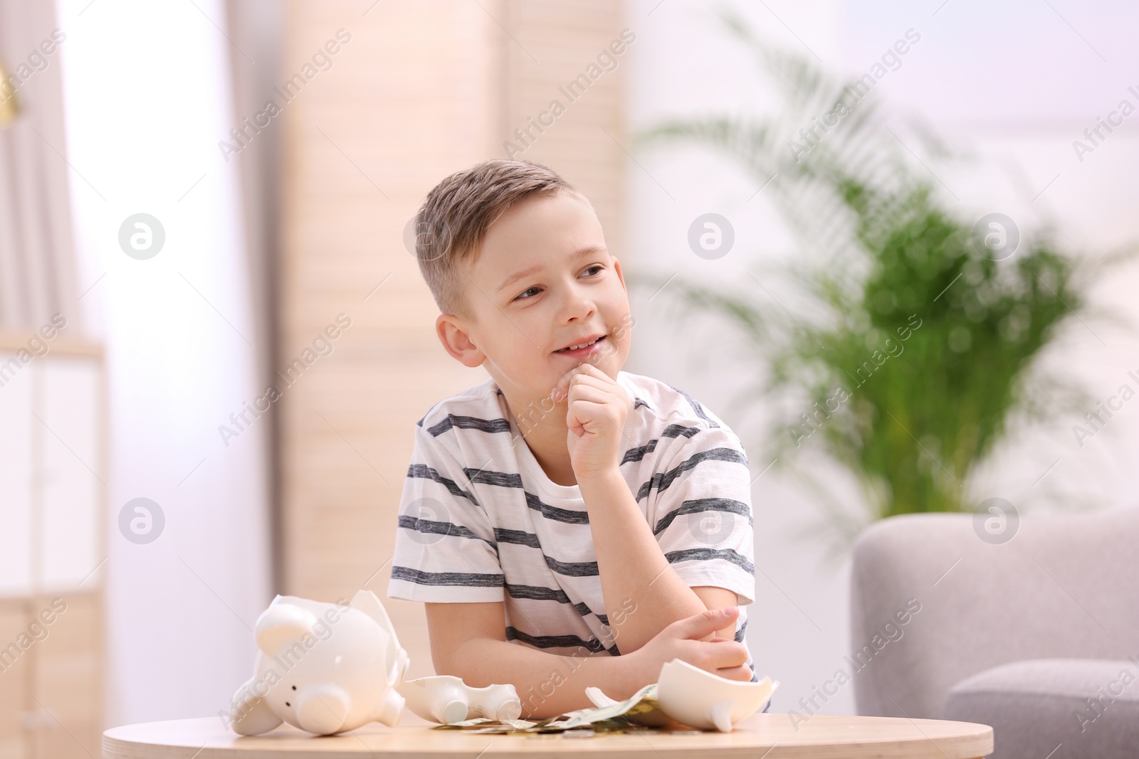 Photo of Little boy with broken piggy bank and money at home