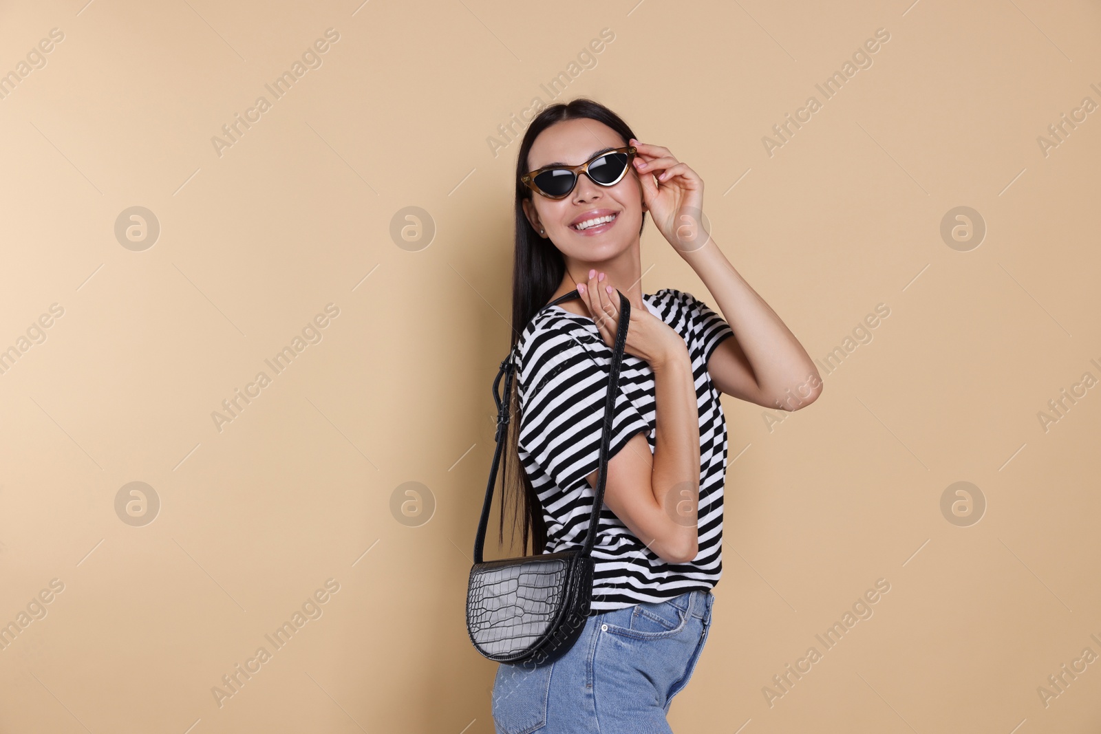 Photo of Beautiful young woman with stylish bag in sunglasses on beige background