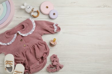 Flat lay composition with baby clothes and accessories on white wooden table. Space for text