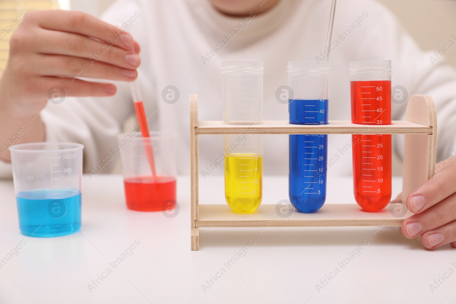 Photo of Girl mixing colorful liquids at white table indoors, closeup. Chemical experiment set for kids