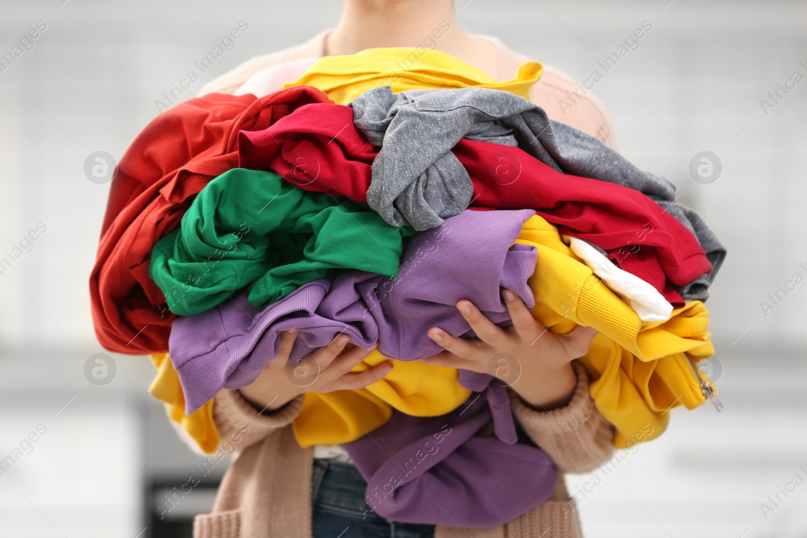 Photo of Woman holding pile of dirty laundry indoors, closeup