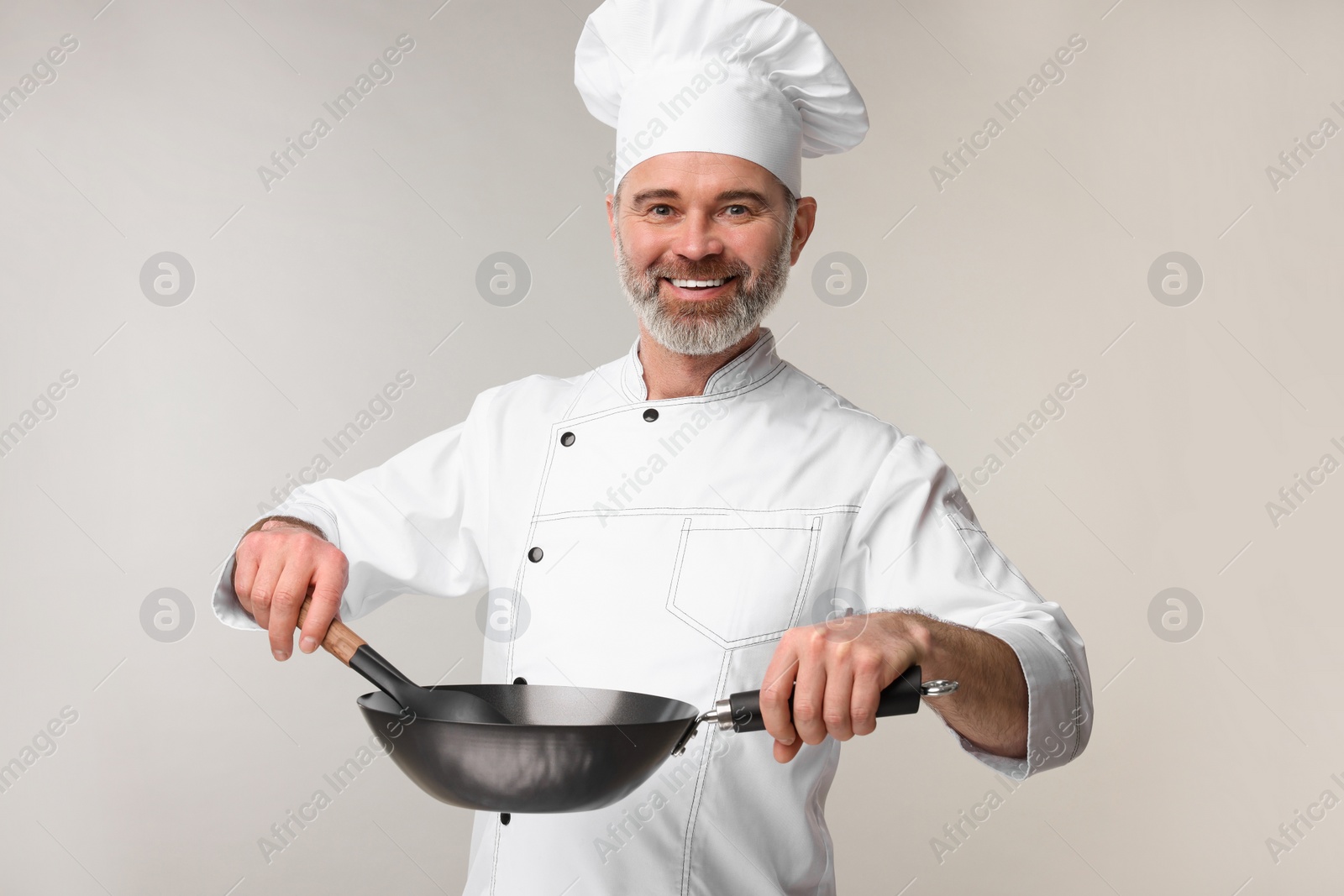 Photo of Happy chef in uniform with wok and spoon on grey background