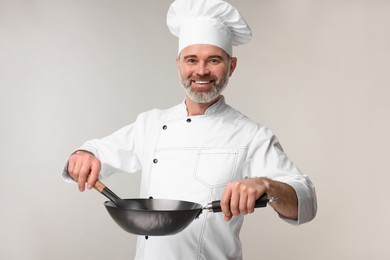 Happy chef in uniform with wok and spoon on grey background