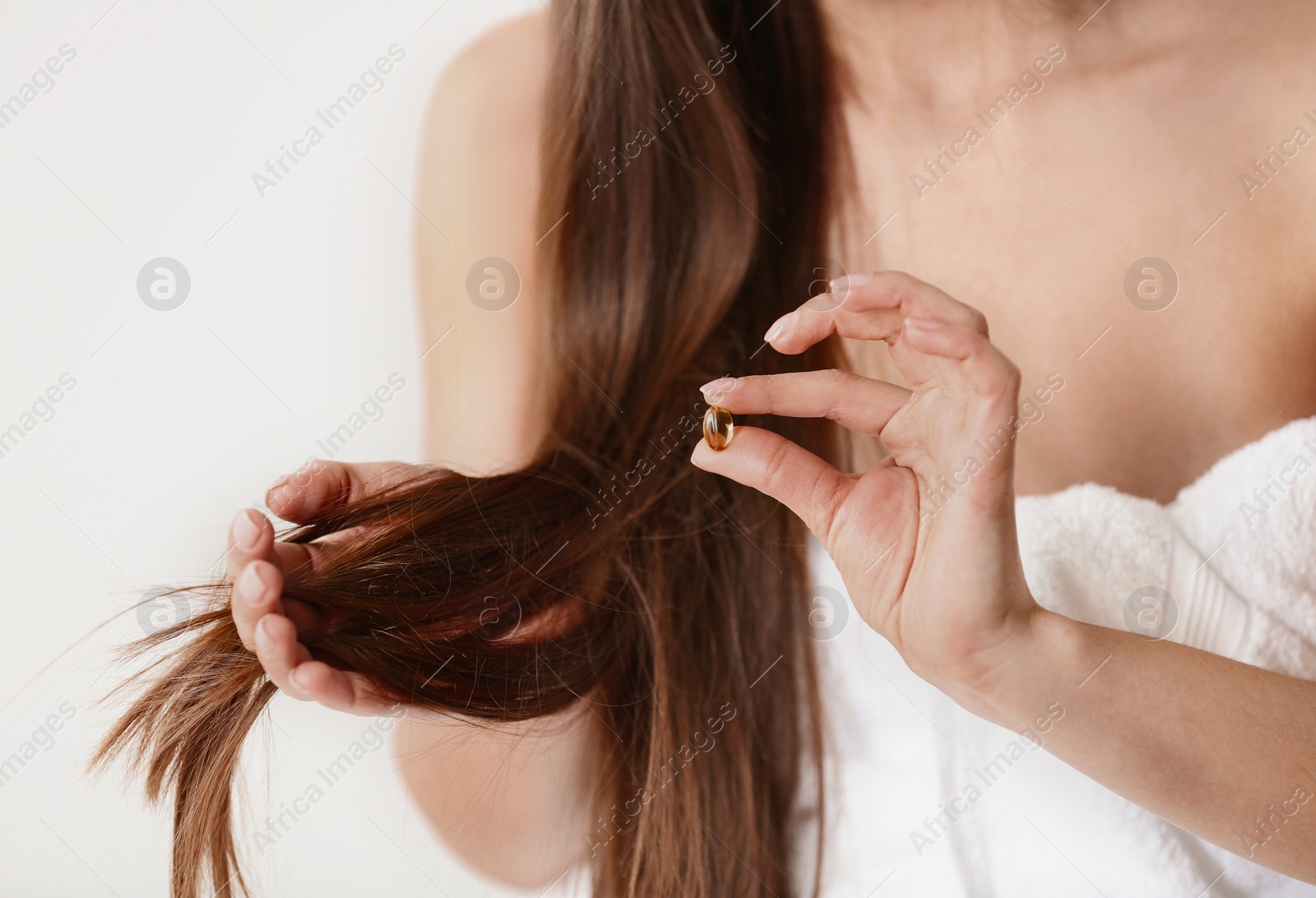 Photo of Woman holding vitamin capsule for hair health on light background, closeup