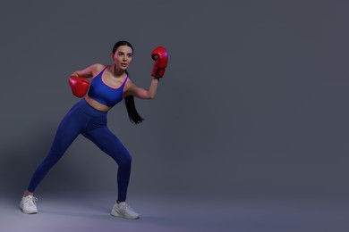 Photo of Beautiful woman wearing boxing gloves in color lights on grey background. Space for text