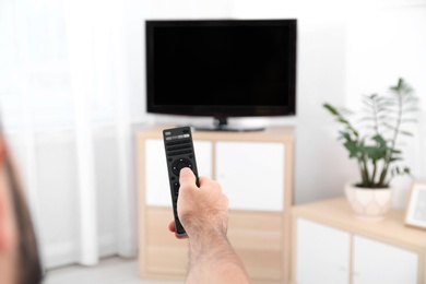 Young man switching channels on modern TV with remote control at home