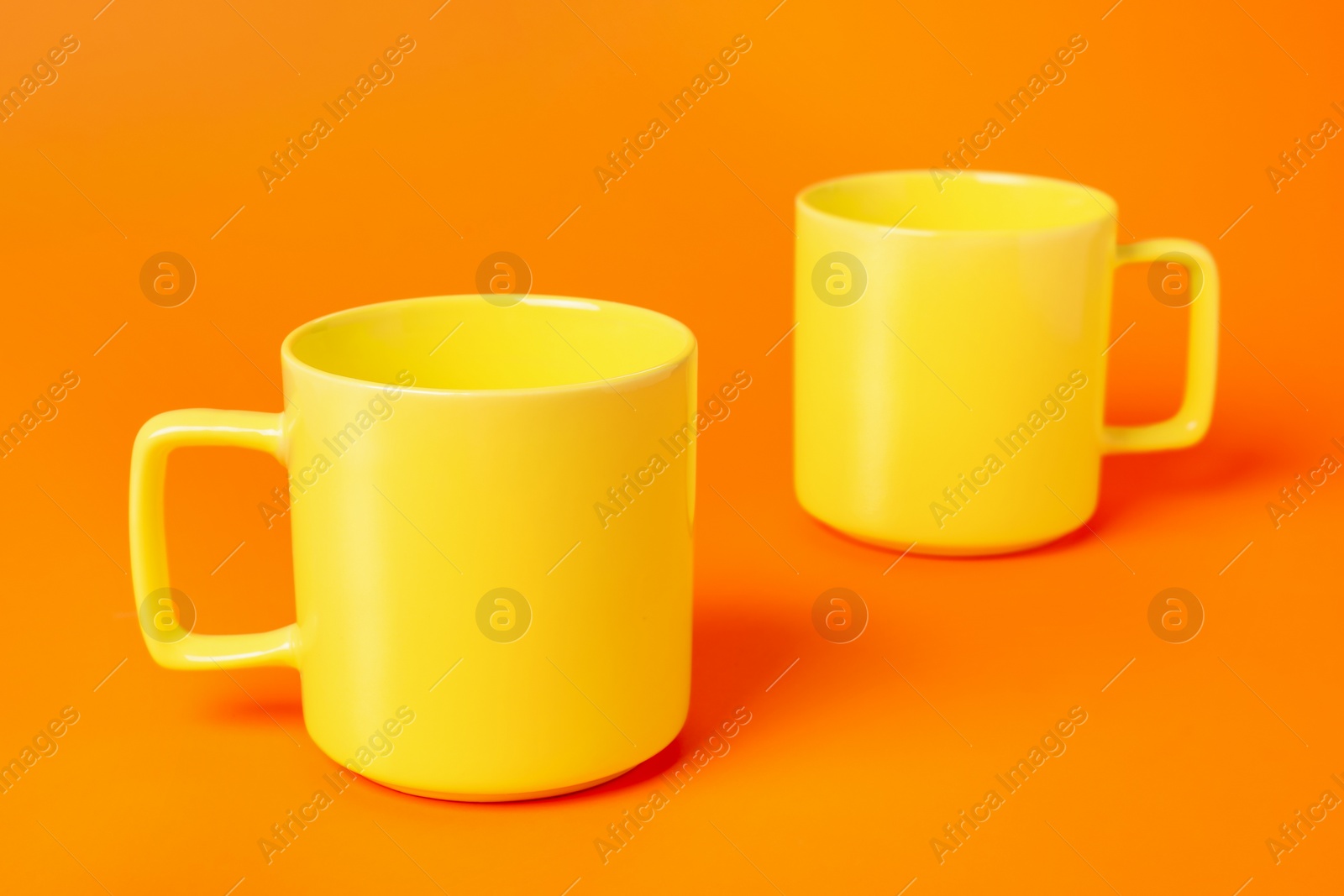 Photo of Two yellow ceramic mugs on orange background