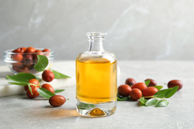 Jojoba oil in glass bottle and seeds on light grey table