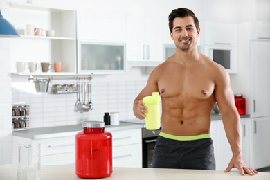 Young shirtless athletic man with protein shake powder in kitchen, space for text