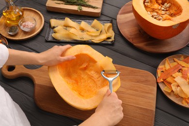 Photo of Woman slicing fresh pumpkin at grey wooden table, closeup