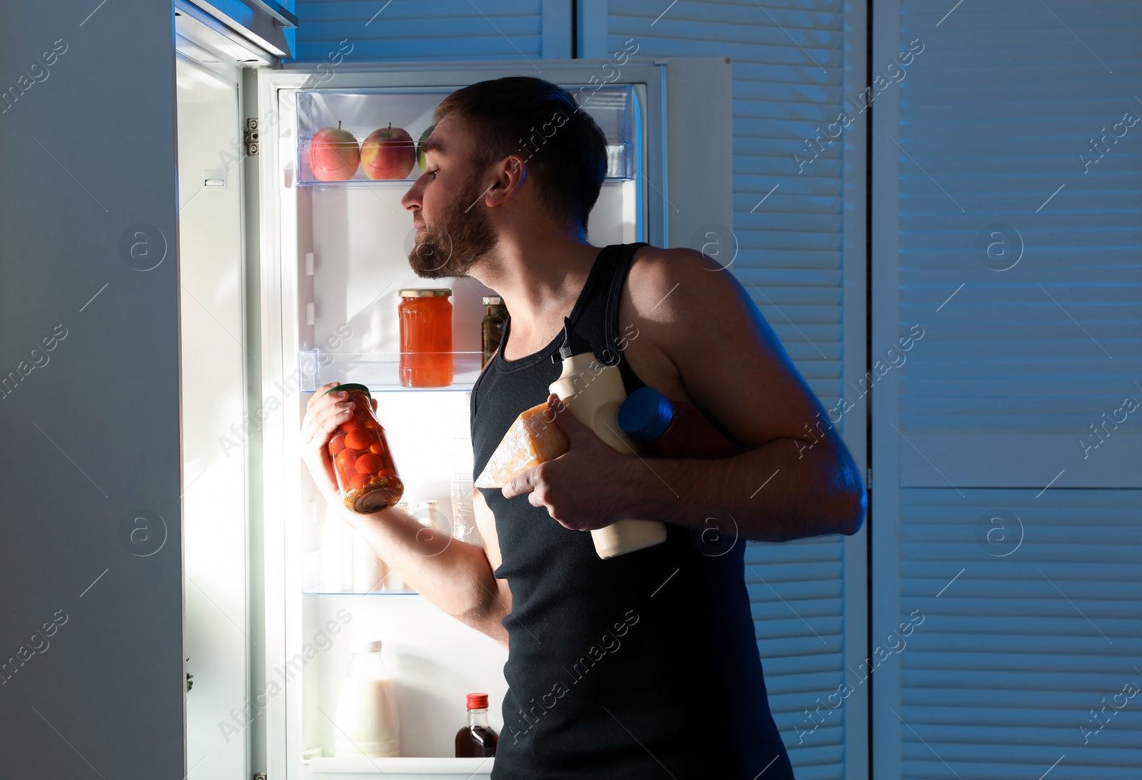 Photo of Man taking products out of refrigerator in kitchen at night