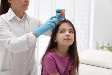 Photo of Doctor using nit comb and spray on little girl indoors. Anti lice treatment