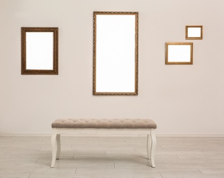 Photo of Frames with empty canvases on wall and bench in modern art gallery. Mockup for design
