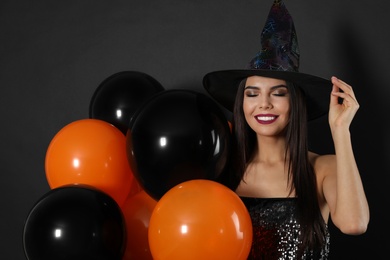 Photo of Beautiful woman wearing witch costume with balloons for Halloween party on black background