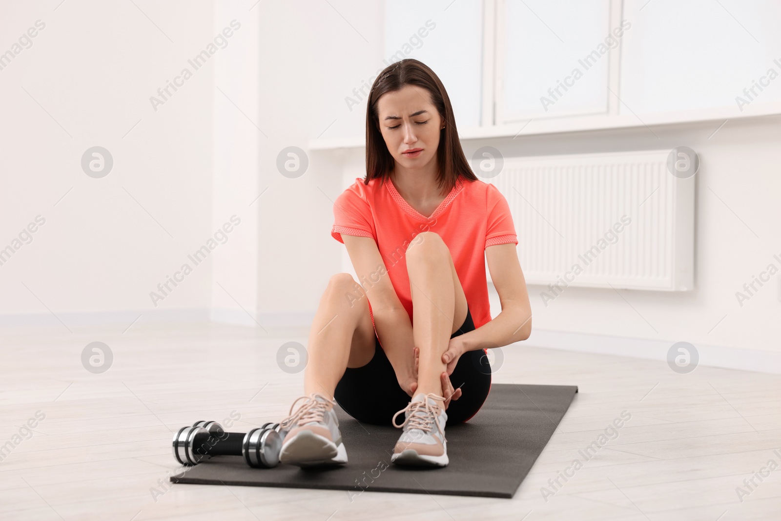 Photo of Young woman suffering from leg pain on exercise mat indoors