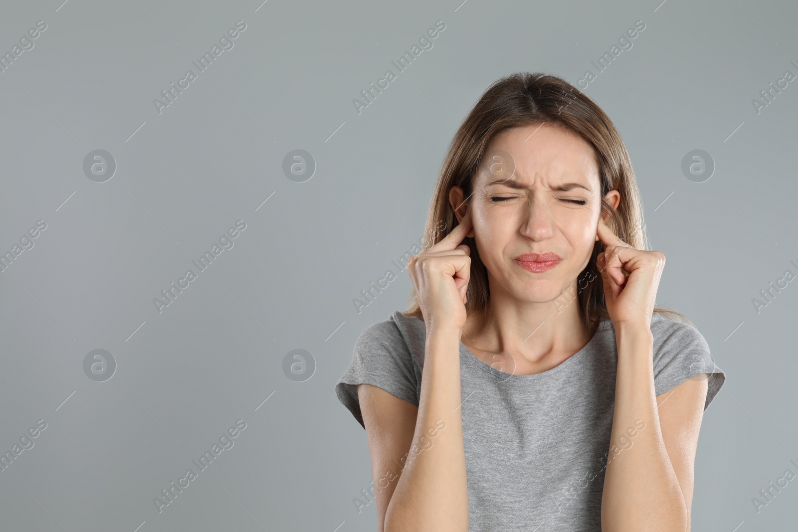 Photo of Emotional young woman covering her ears with fingers on grey background. Space for text