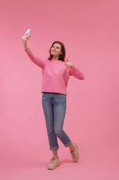 Beautiful woman taking selfie on pink background