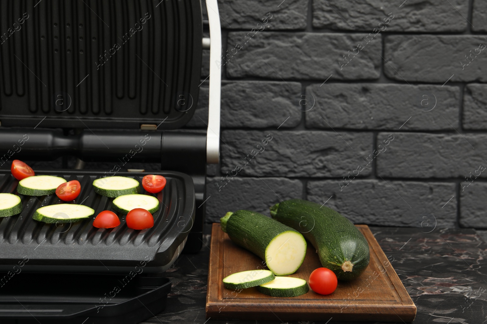 Photo of Electric grill with vegetables on black marble table