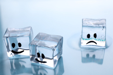 Photo of Ice cubes with drawn faces on light background, closeup. Concept of jealousy