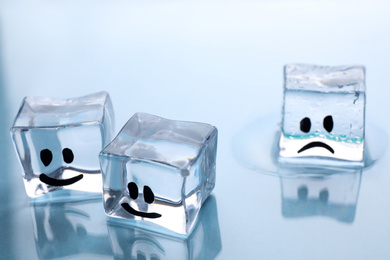 Ice cubes with drawn faces on light background, closeup. Concept of jealousy