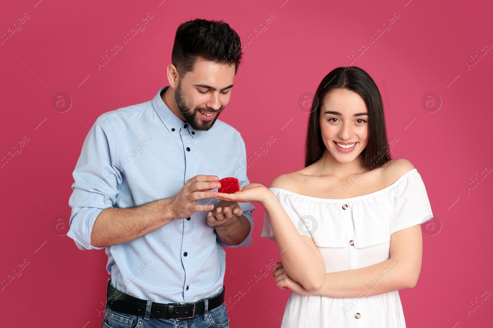 Photo of Young woman with engagement ring making marriage proposal to her boyfriend on crimson background