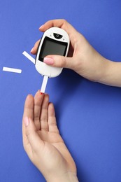 Photo of Diabetes. Woman checking blood sugar level with glucometer on blue background, top view