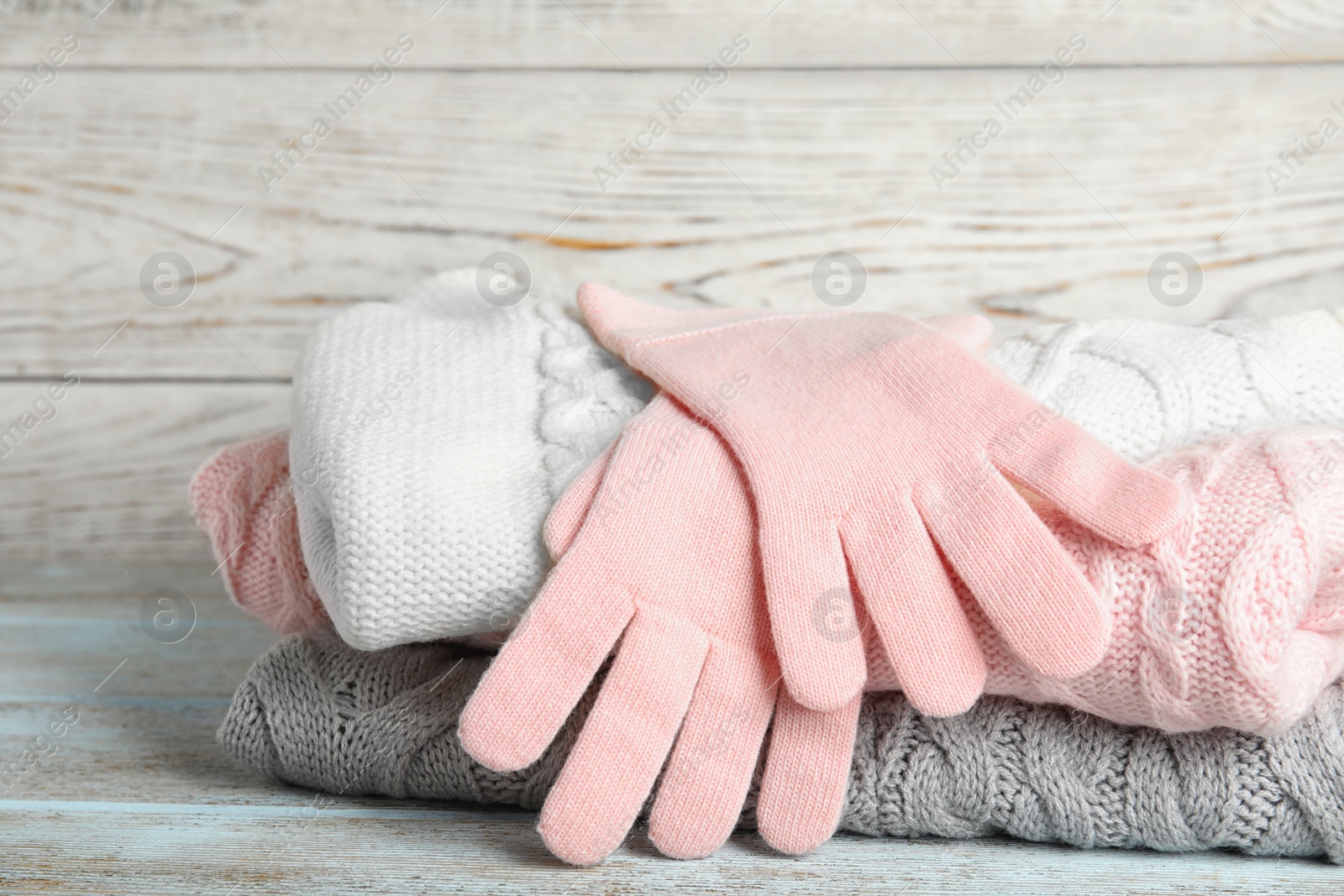 Photo of Stacked sweaters and gloves on wooden table, closeup. Autumn clothes