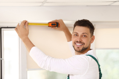 Image of Handyman with tape measure installing roller window blind indoors