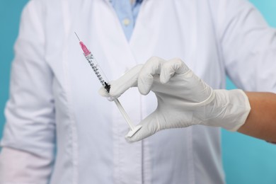 Doctor holding syringe on light blue background, closeup