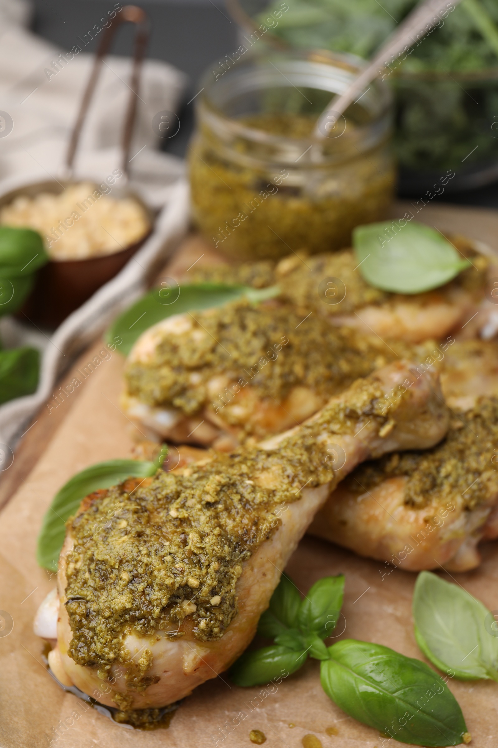 Photo of Delicious fried chicken drumsticks with pesto sauce and basil on table, closeup