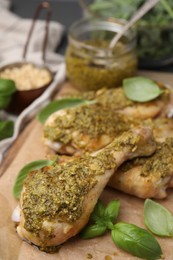 Photo of Delicious fried chicken drumsticks with pesto sauce and basil on table, closeup