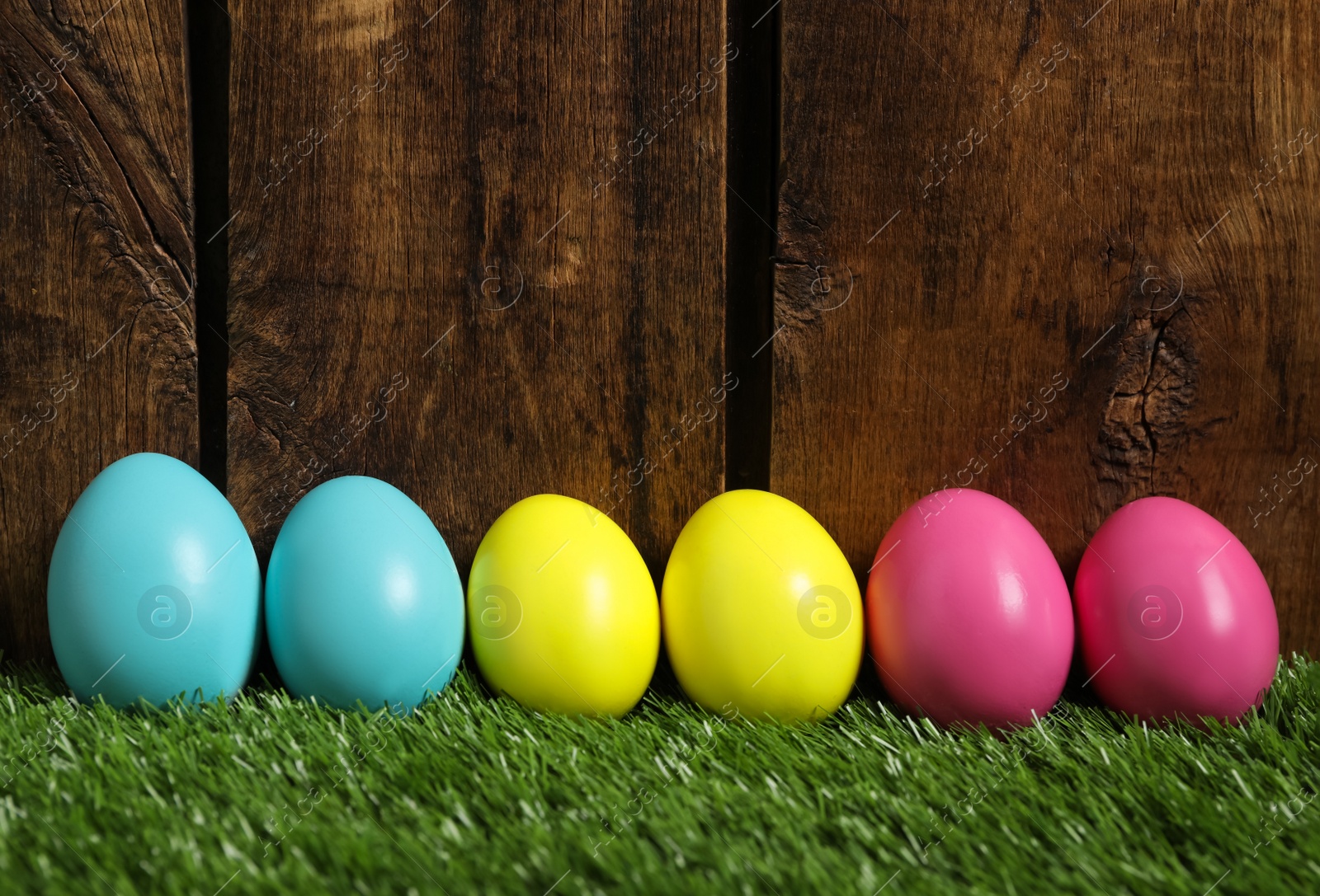 Photo of Bright Easter eggs on green grass against wooden background
