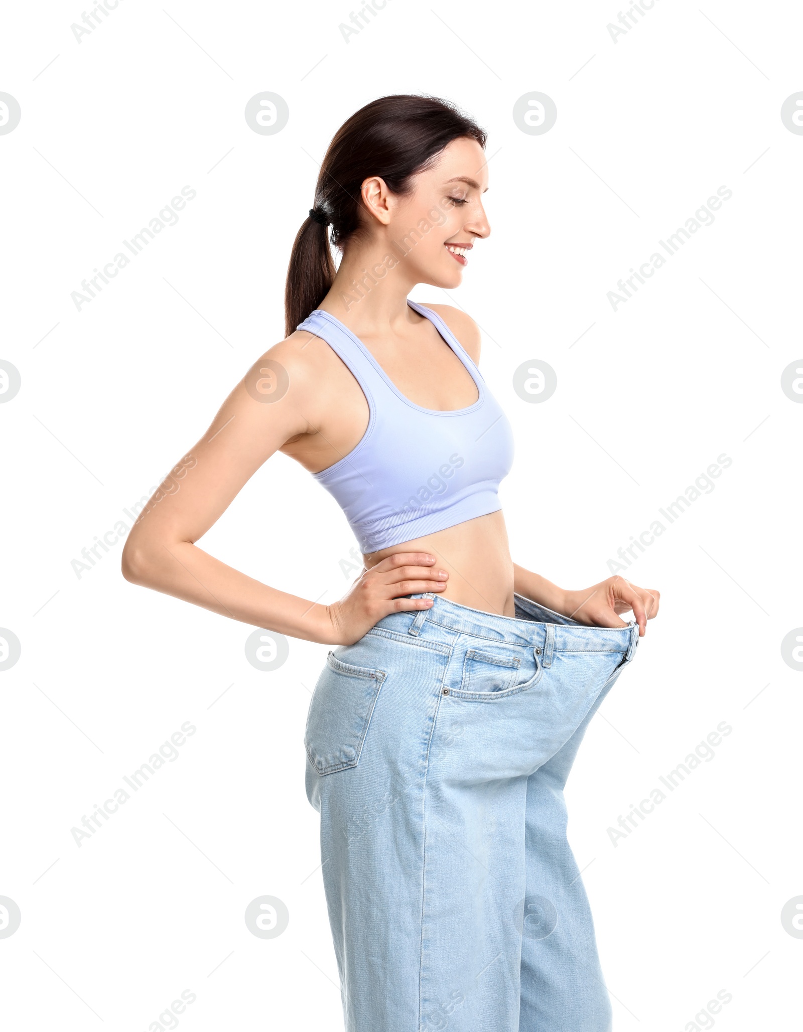 Photo of Happy young woman in big jeans showing her slim body on white background