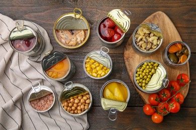 Open tin cans with different products on wooden table, flat lay