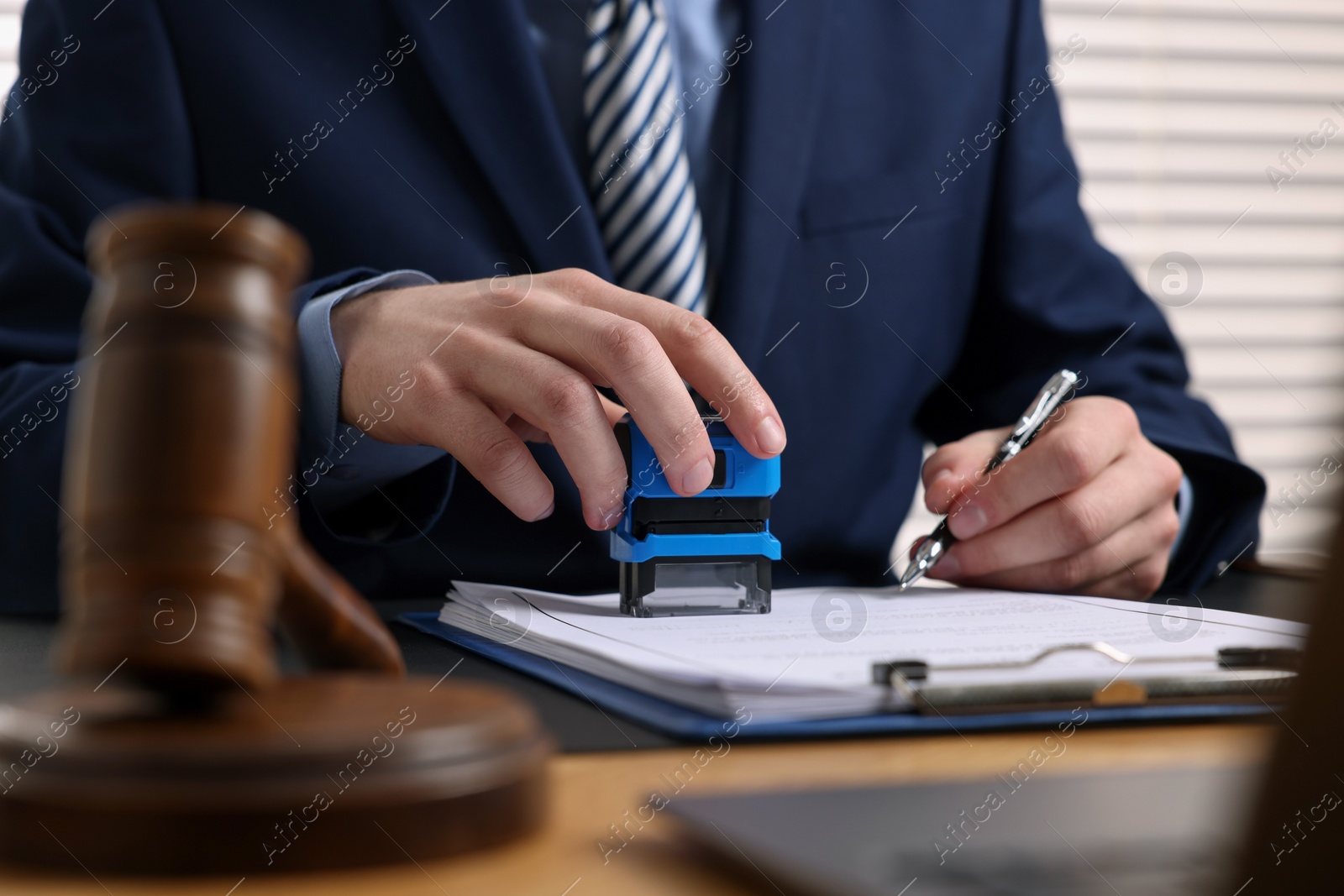 Photo of Notary with pen stamping document at table in office, closeup