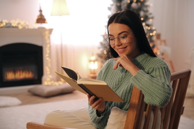 Photo of Young woman reading book at home. Christmas celebration