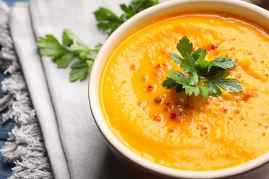 Delicious pumpkin cream soup with parsley and spices in bowl on table, closeup