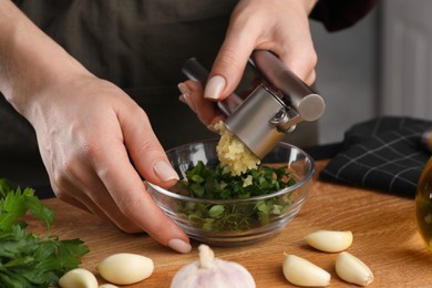 Woman squeezing garlic with press at wooden table, closeup