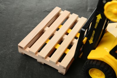 Photo of Toy forklift with wooden pallet on black table, closeup