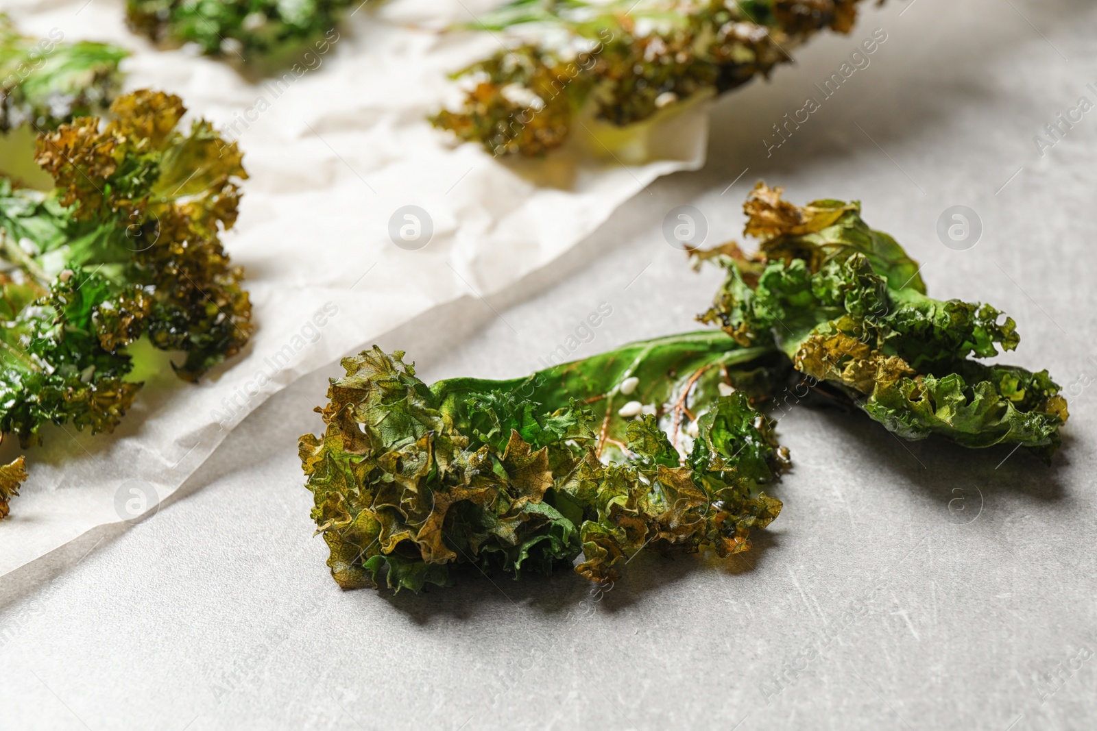 Photo of Tasty baked kale chips on grey table, closeup