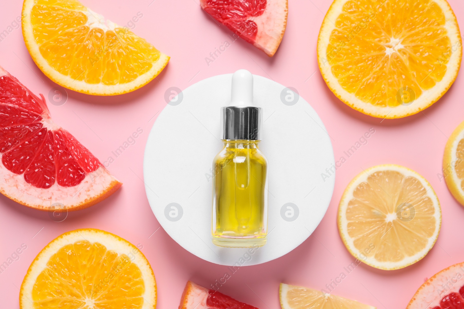 Photo of Bottle of cosmetic serum and citrus fruit slices on pink background, flat lay