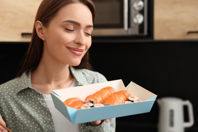 Photo of Beautiful young woman with box of sushi rolls in kitchen