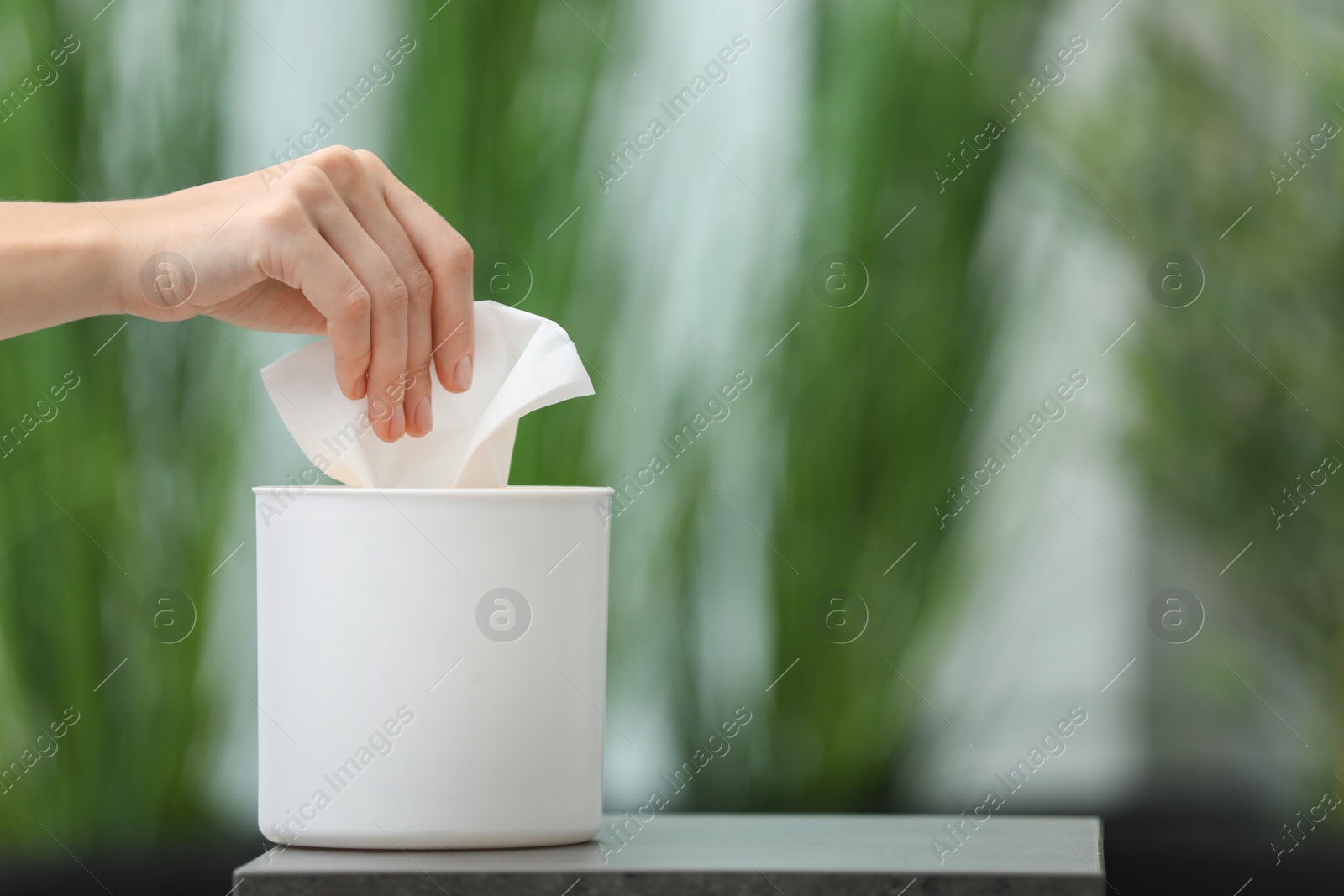 Photo of Woman taking paper tissue from holder on blurred background, closeup. Space for text