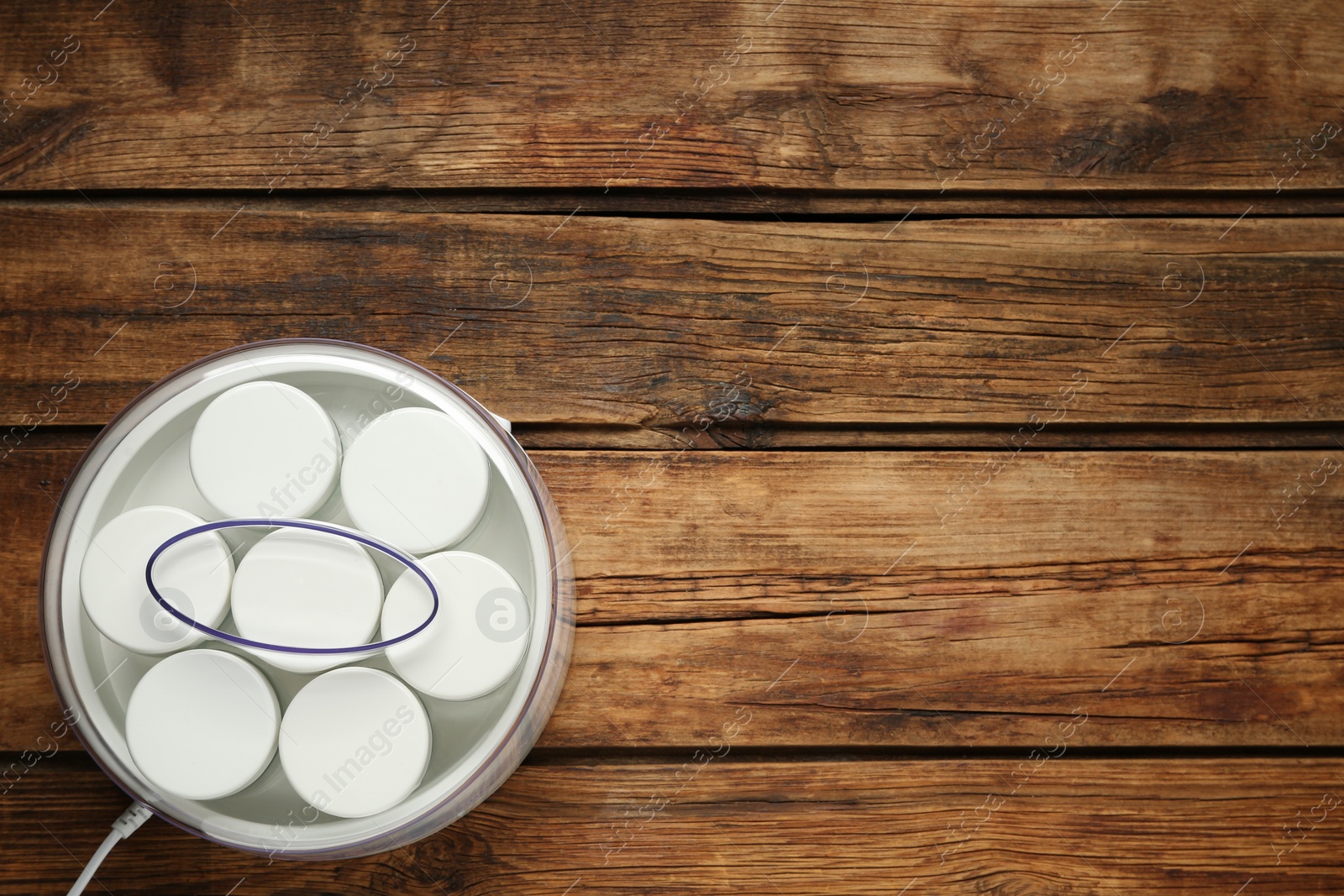 Photo of Modern yogurt maker with jars on wooden table, top view. Space for text