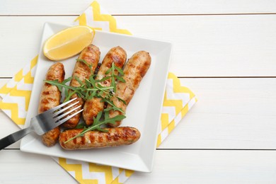 Tasty grilled sausages served with lemon and arugula on white wooden table, top view. Space for text