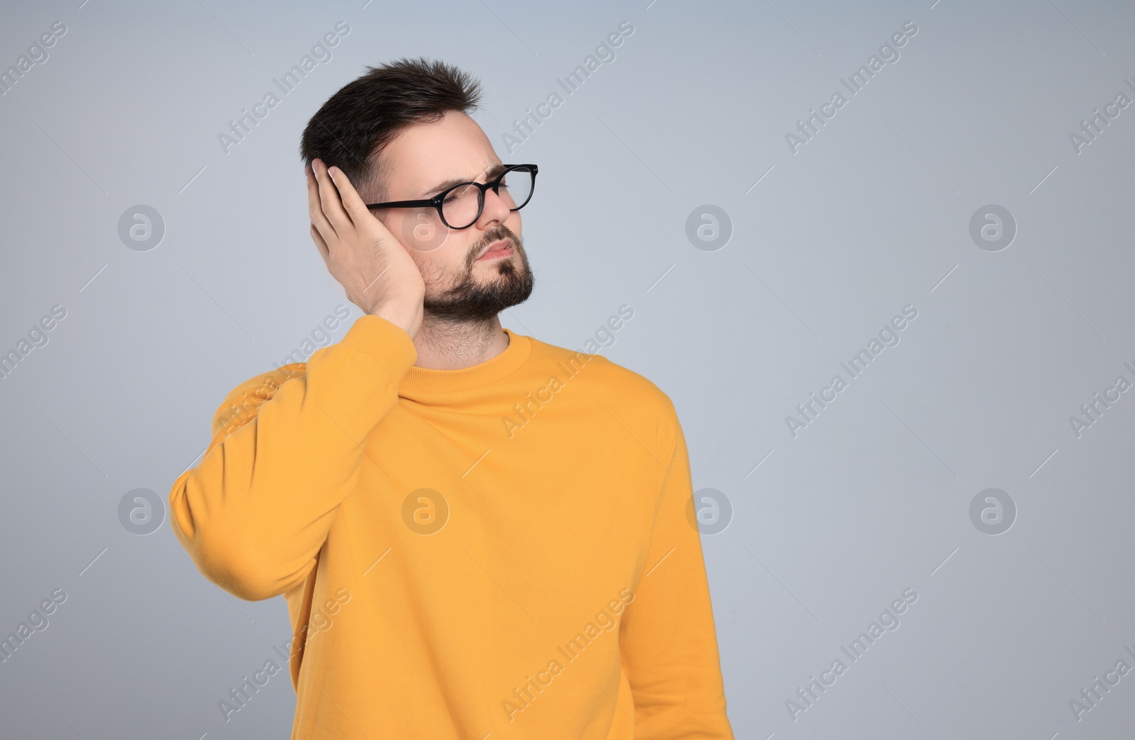 Photo of Young man suffering from ear pain on light grey background. Space for text